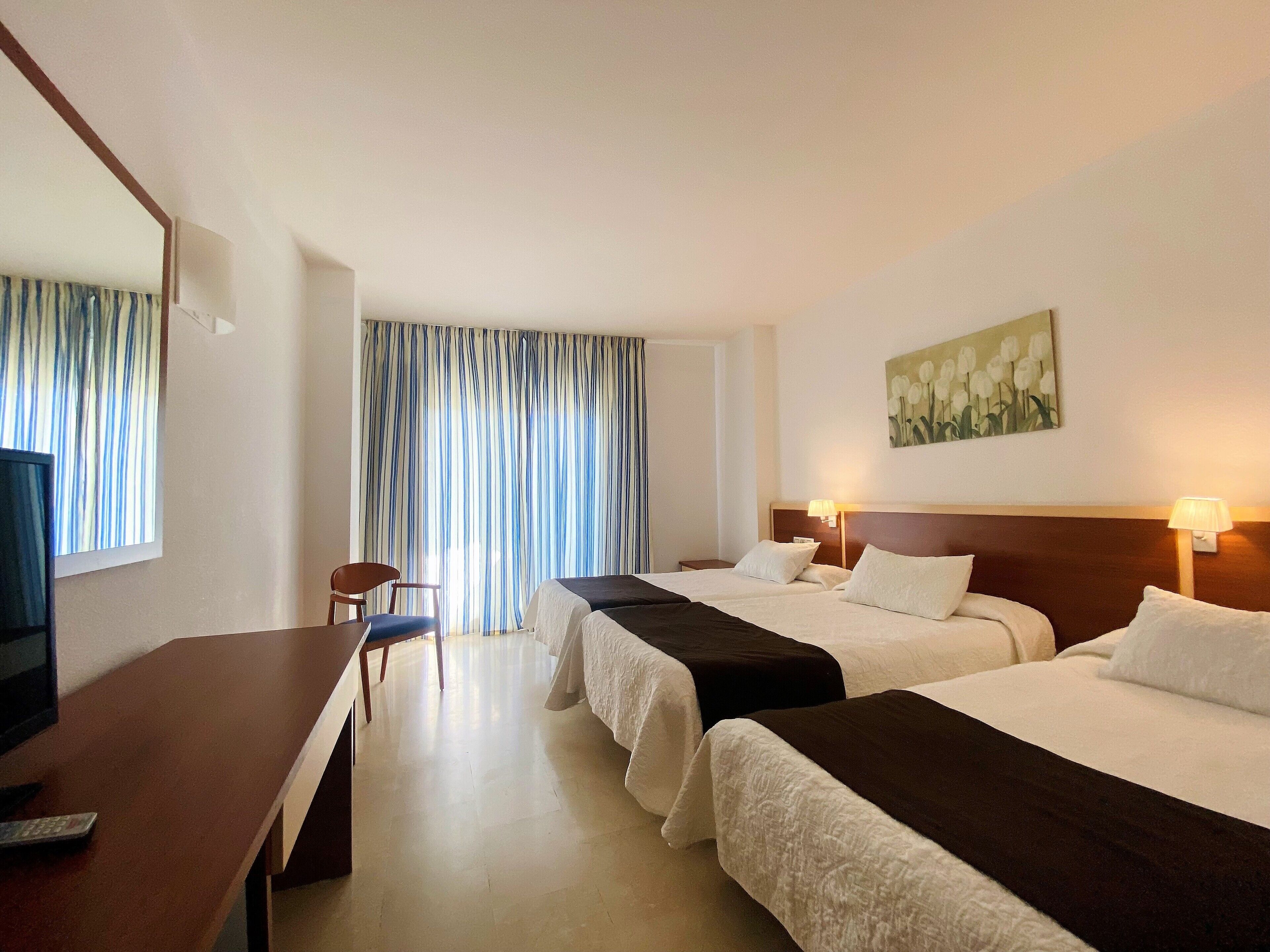 Habitación de hotel con dos camas, un escritorio con silla, un televisor y un cuadro en la pared.