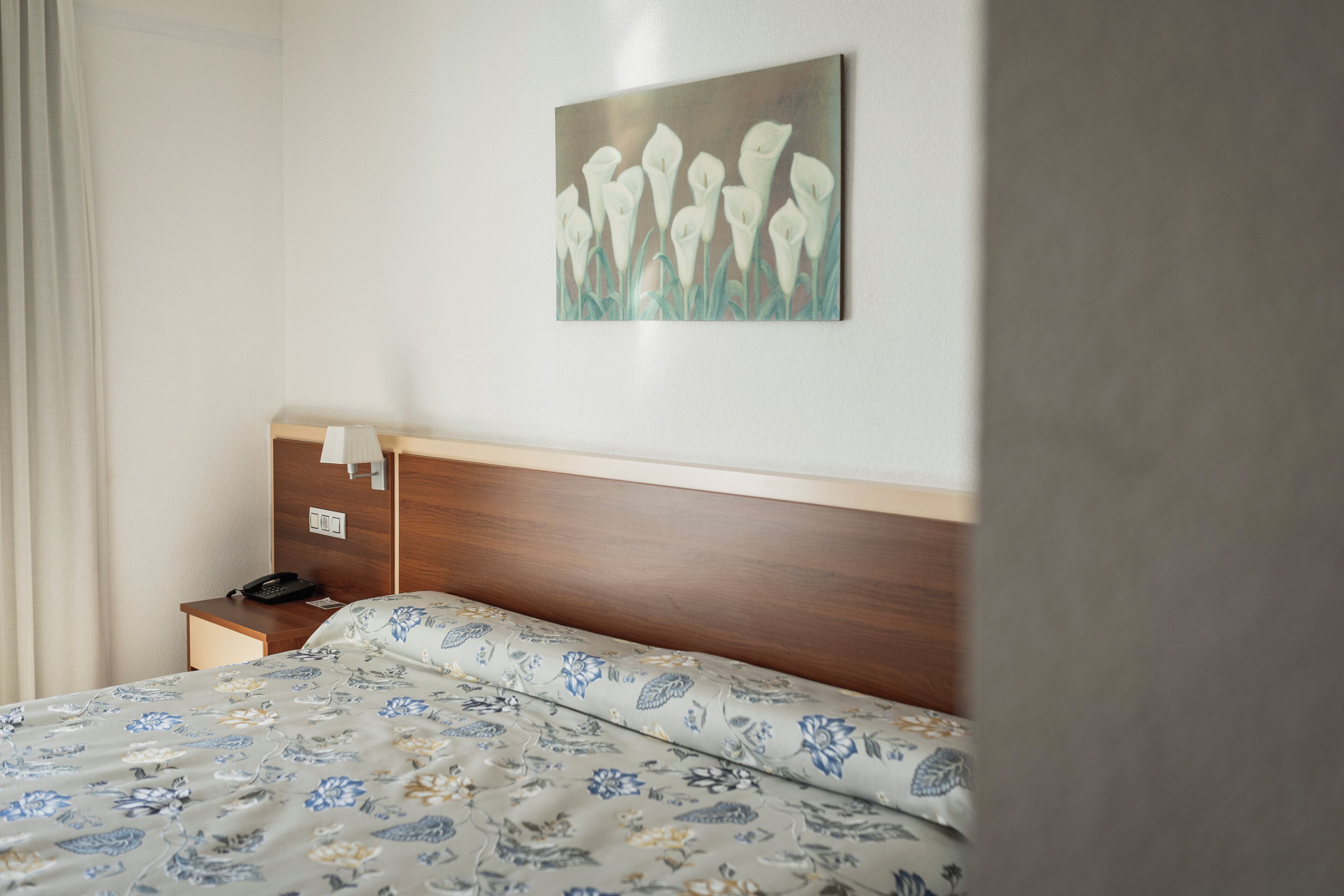 Habitación de hotel con cama, mesita de noche, teléfono y un cuadro colgado en la pared.