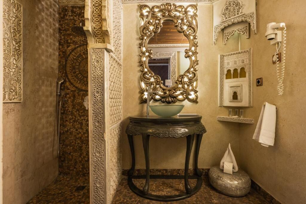 A bathroom with an ornate mirror, a sink with a bowl, a towel dispenser, and a wall-mounted phone.