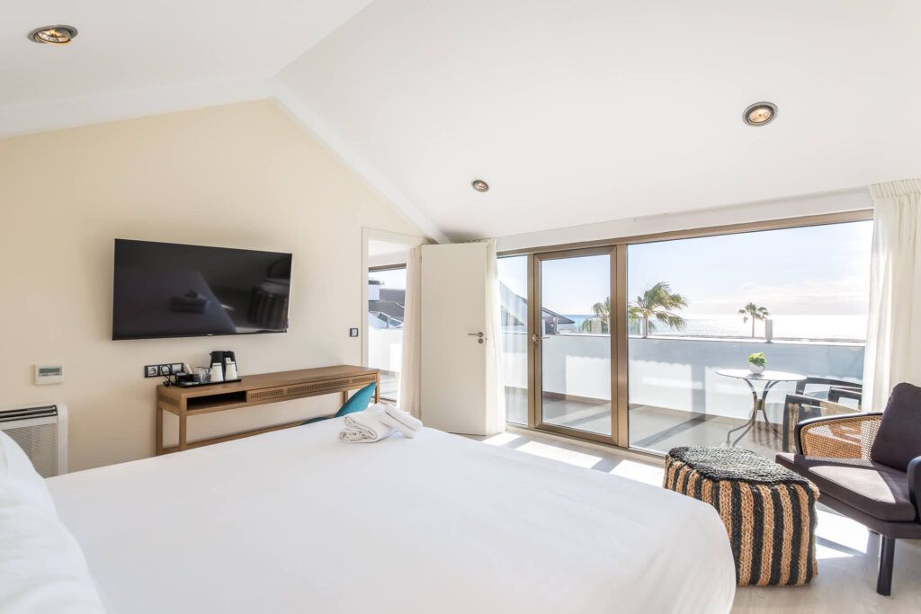 Een hotelkamer met een bed, televisie, bureau, stoel, balkon met tafel en stoelen, en uitzicht op zee.