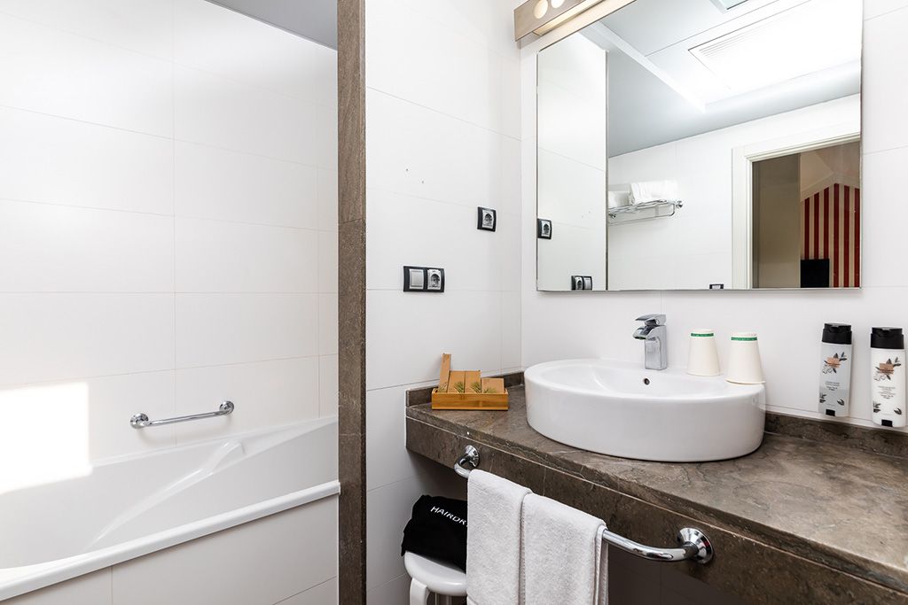 A modern bathroom with a bathtub, a large mirror, a sink, and toiletries.