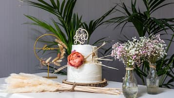 Un pastel blanco con la inscripción 'love', rodeado de elementos decorativos como una flor rosa, plumas de pampa y dos jarrones de vidrio con flores.