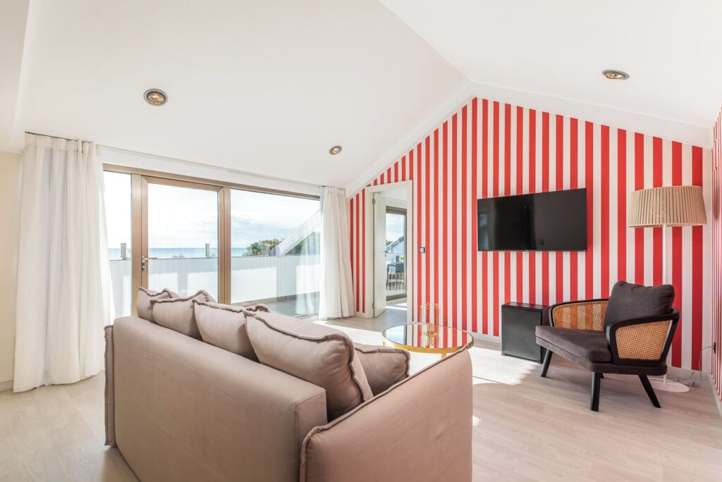 A modern living room with a sofa, a chair, a TV mounted on the wall, and a balcony with a view.