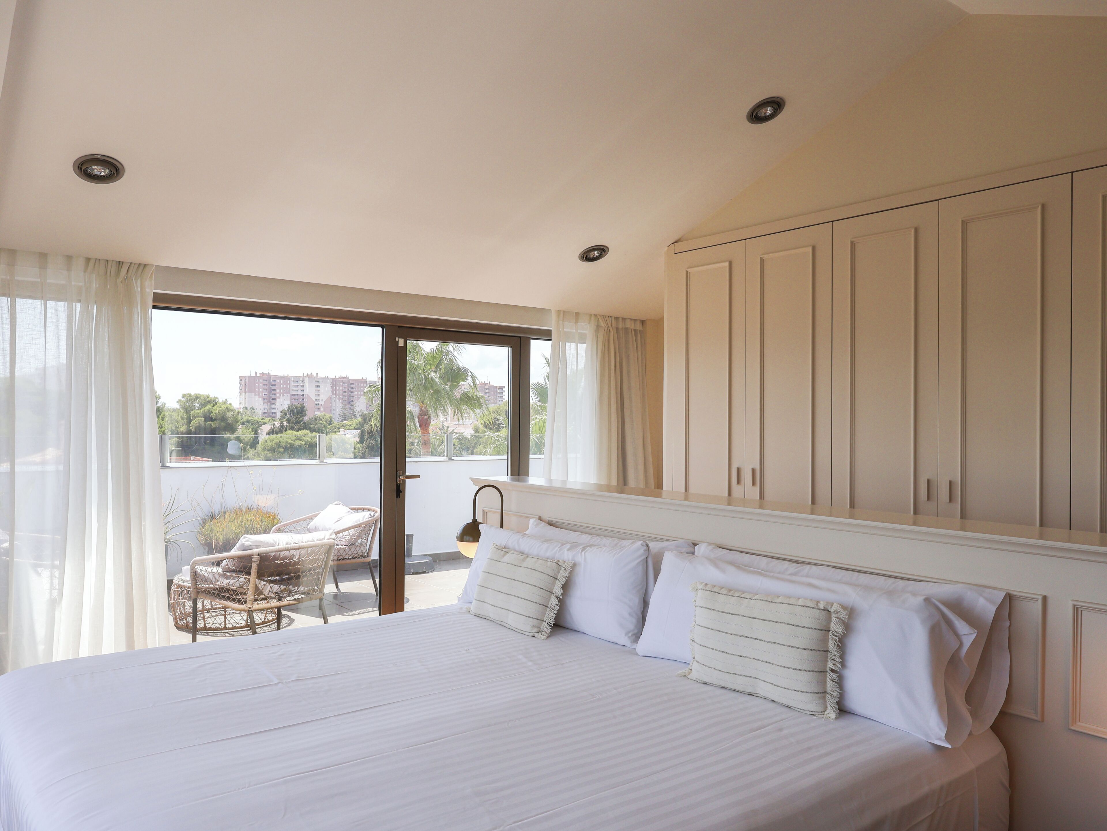 Un dormitorio con cama, una silla y vistas al exterior.
