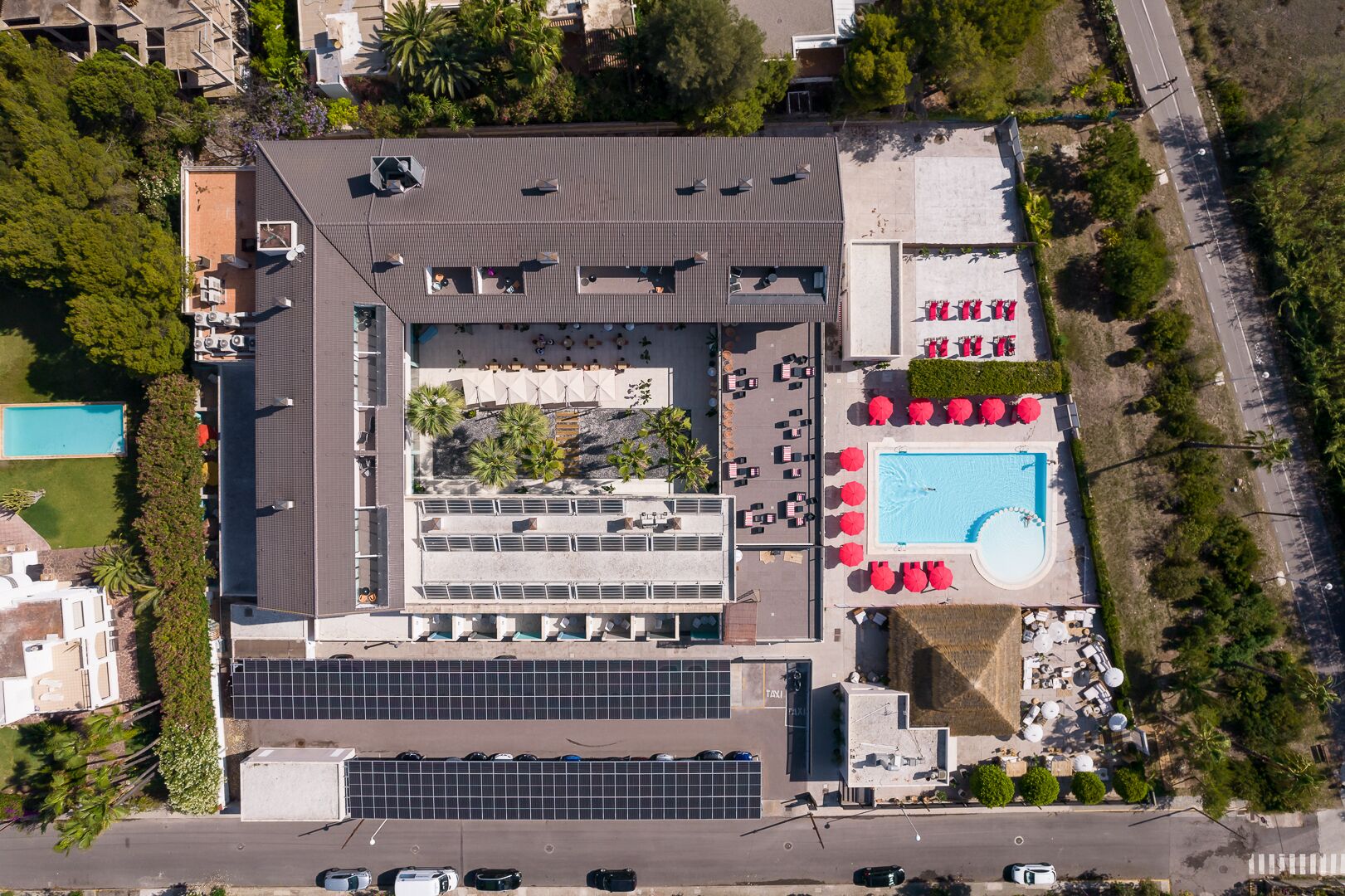 An aerial view of a hotel with a rooftop pool, a parking area, and a landscaped courtyard.