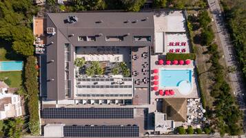 An aerial view of a hotel with a rooftop pool, a parking area, and a landscaped courtyard.