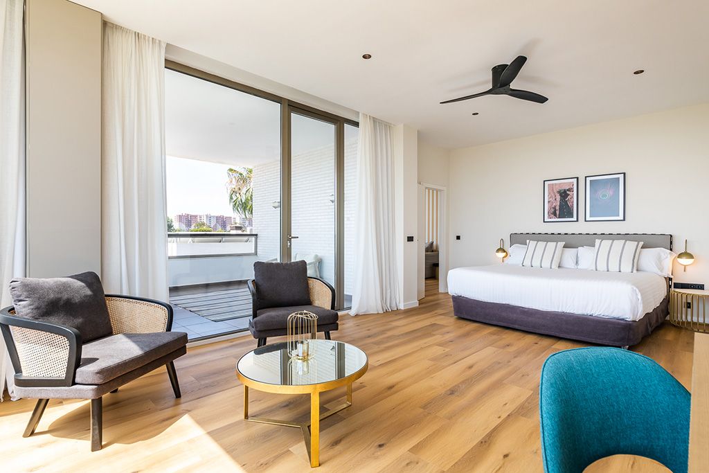 Una habitación de hotel moderna con una cama grande, un área de descanso con una mesa redonda y un balcón con cortinas.