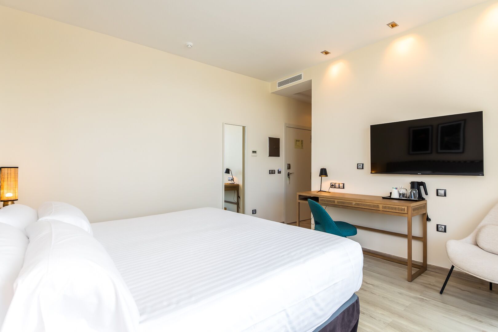 A hotel room with a large bed, a desk, a chair, a TV mounted on the wall, and a mirror.