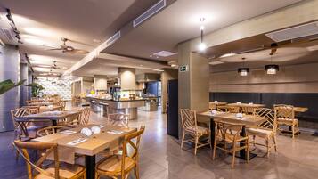 A modern restaurant with wooden tables and chairs, a central bar area, and ceiling fans.