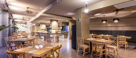 A modern restaurant with wooden tables and chairs, a central bar area, and ceiling fans.