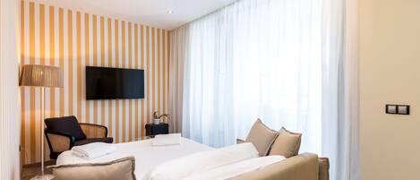 Una habitación de hotel moderna con una cama grande, un televisor de pantalla plana, un escritorio con una silla y un ventanal con cortinas translúcidas.