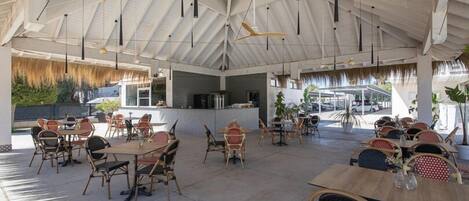 An open-air dining area with tables and chairs, a bar counter, and a view of the street.