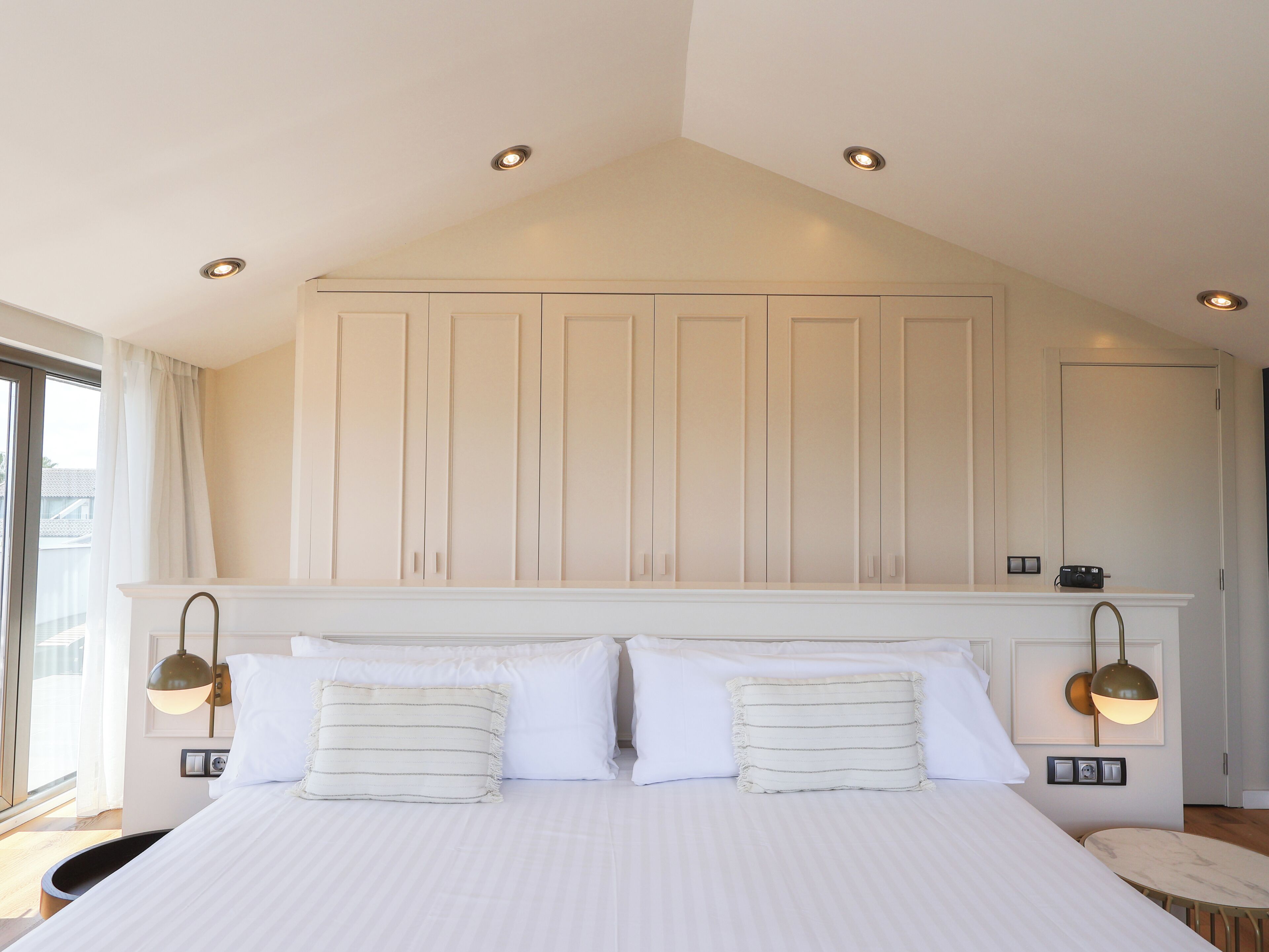 Une chambre avec un grand lit, un plafond doté d’un éclairage encastré et une vue sur l’extérieur par une fenêtre.