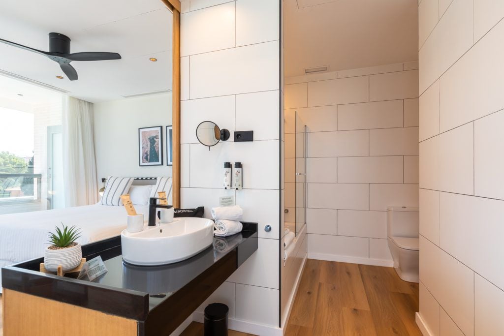 Un baño moderno con un espejo grande, un lavamanos blanco y una zona de ducha.