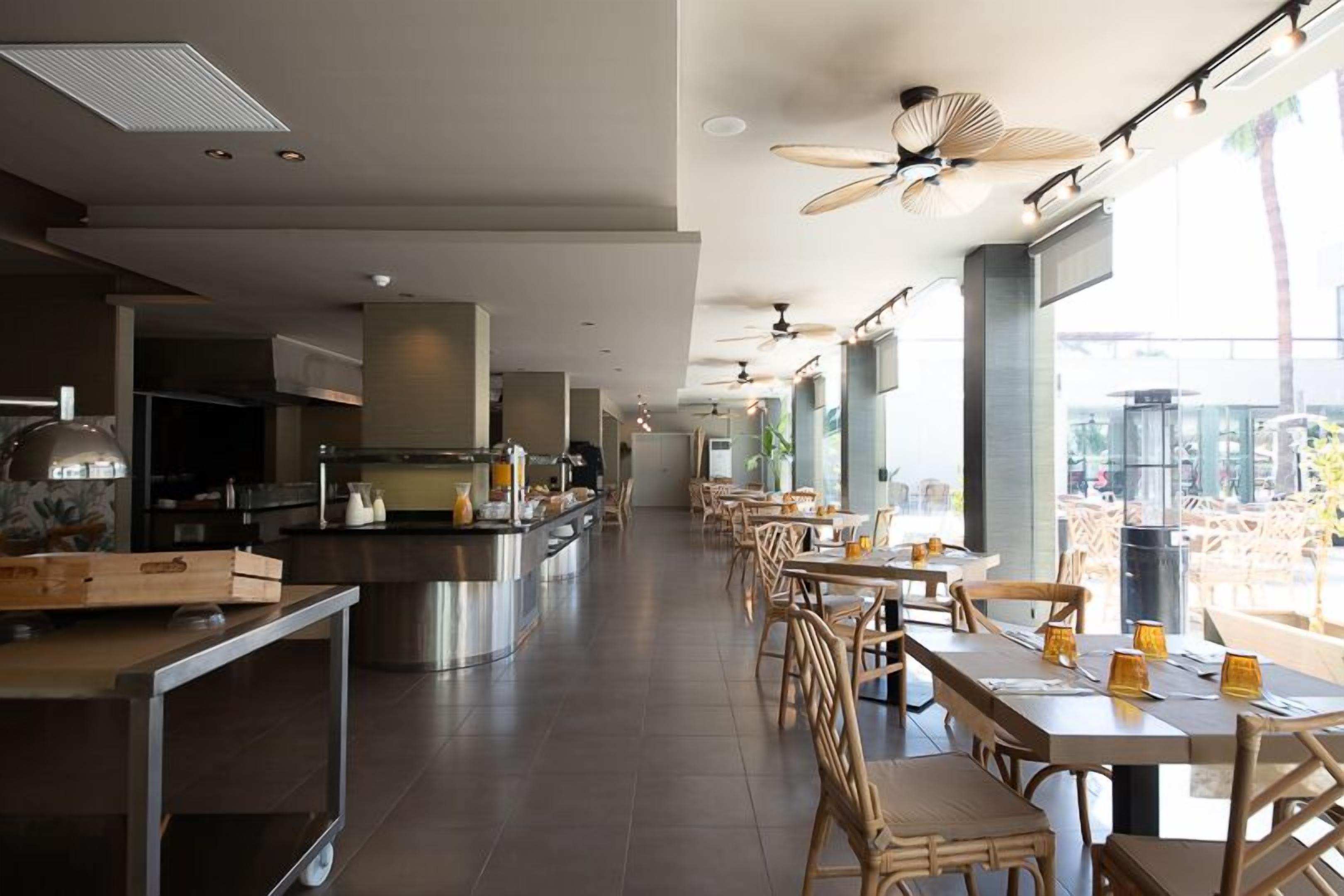 A modern restaurant with a long counter, wooden chairs, and large windows.