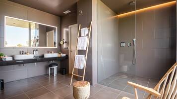 A modern bathroom with a large mirror, two sinks, a shower, and a wooden chair.