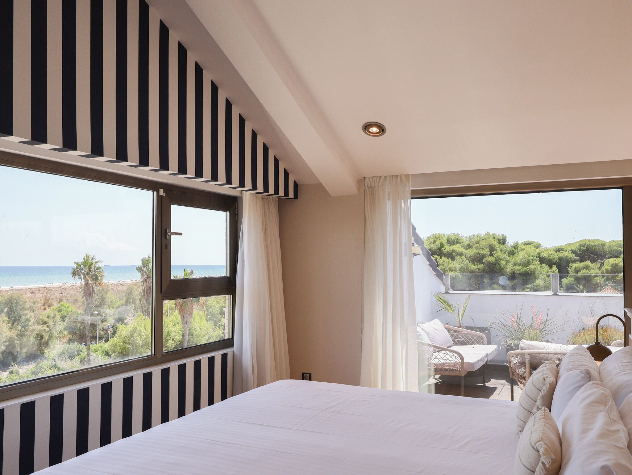 A bedroom with a large bed, a view of the sea, and a balcony with outdoor seating.