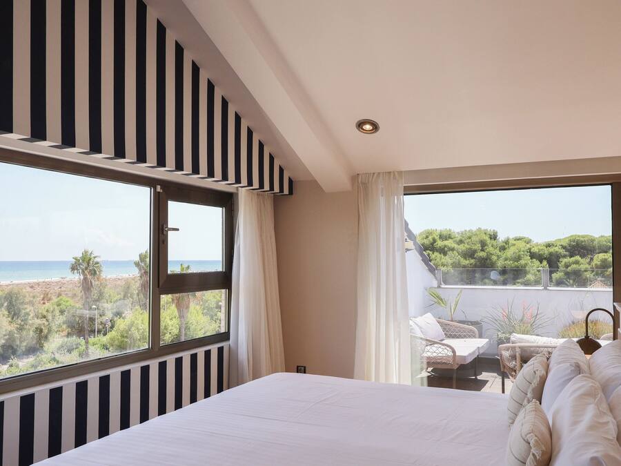 Un dormitorio con una cama grande, vista al mar y un balcón con mobiliario exterior.