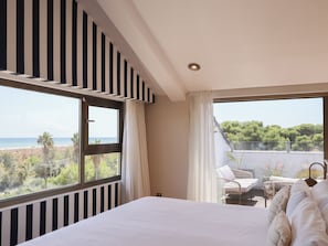 Un dormitorio con una cama grande, vista al mar y un balcón con mobiliario exterior.