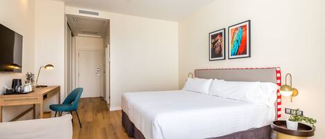 Ein modernes Hotelzimmer mit einem großen Bett, einem Schreibtisch mit Stuhl, einem Fernseher und zwei gerahmten Kunstwerken an der Wand.