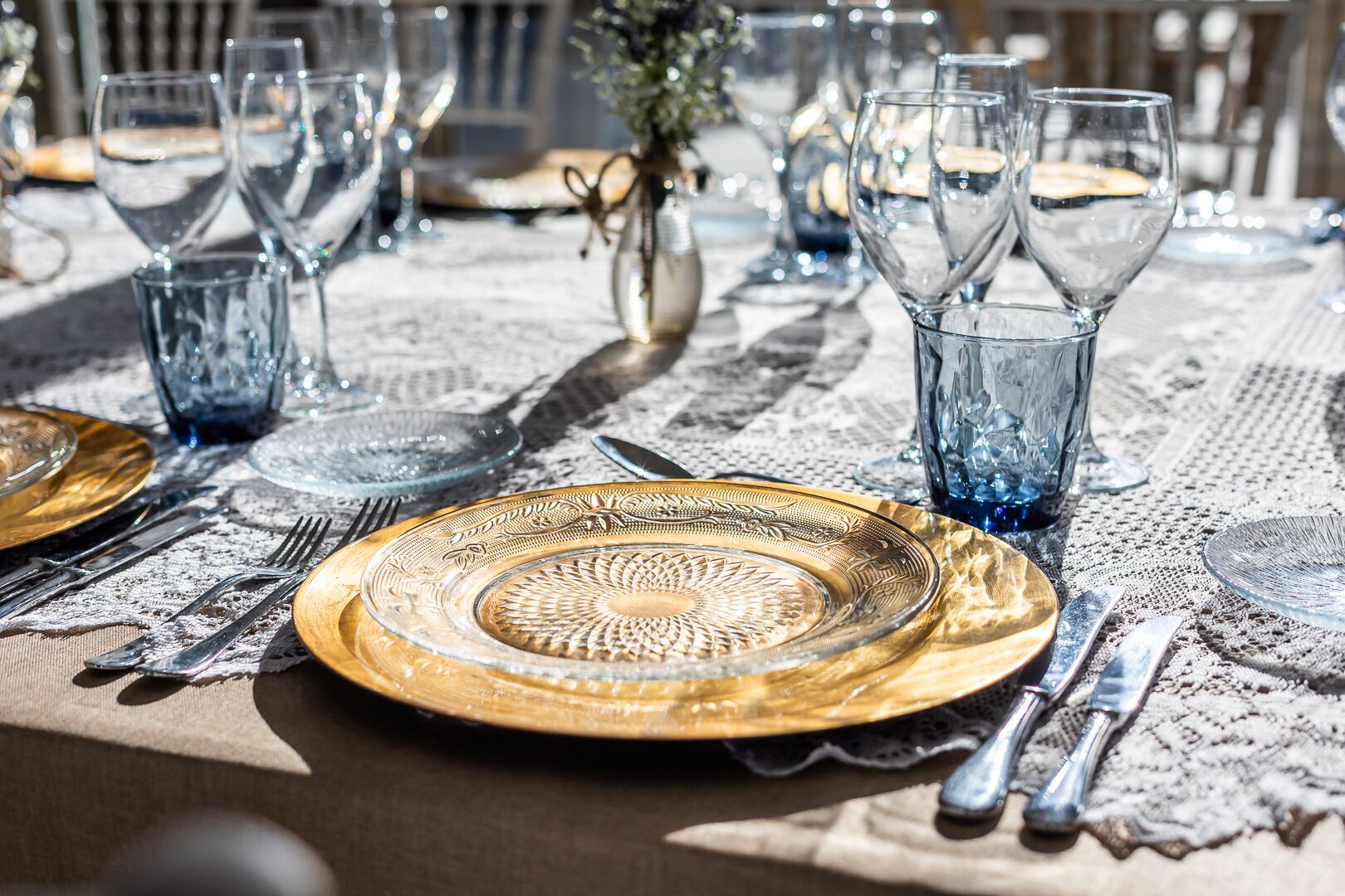 Una mesa dispuesta con cristalería transparente y platos con detalles dorados, lo que sugiere una presentación formal para el servicio de alimentos.