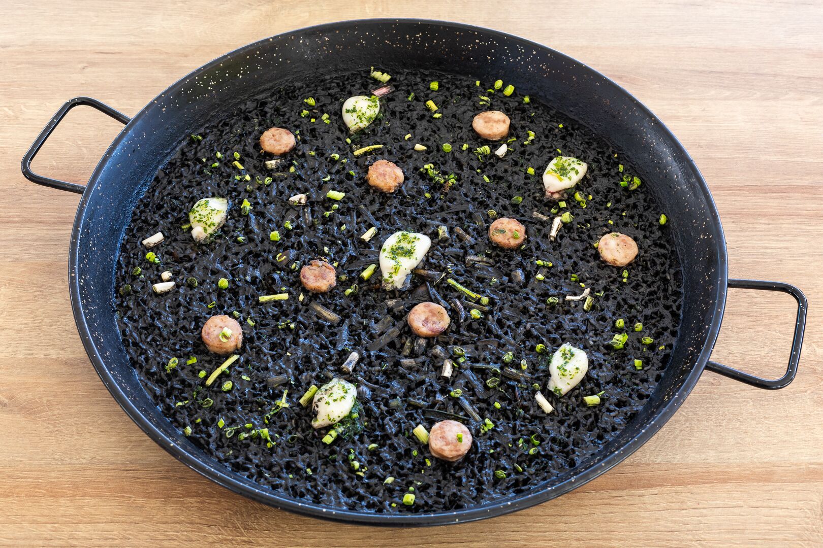 Een zwarte pan met eten, waaronder zwarte rijst en kleine, ronde objecten, op een houten ondergrond.