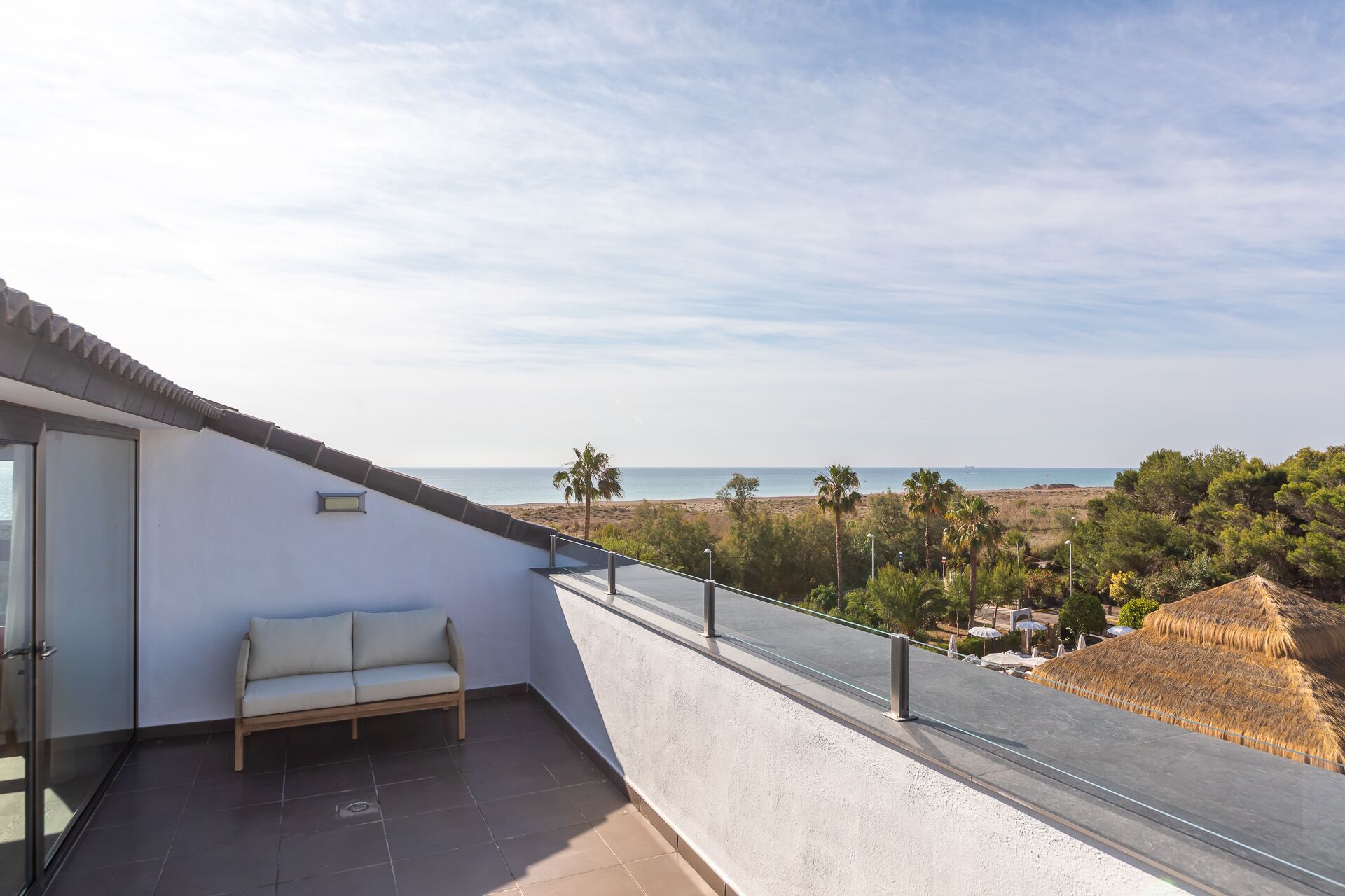 Un balcone con divano, una porta in vetro e vista sulla spiaggia e sull'oceano.