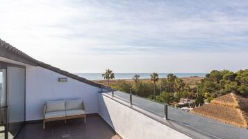 Un balcone con divano, una porta in vetro e vista sulla spiaggia e sull'oceano.