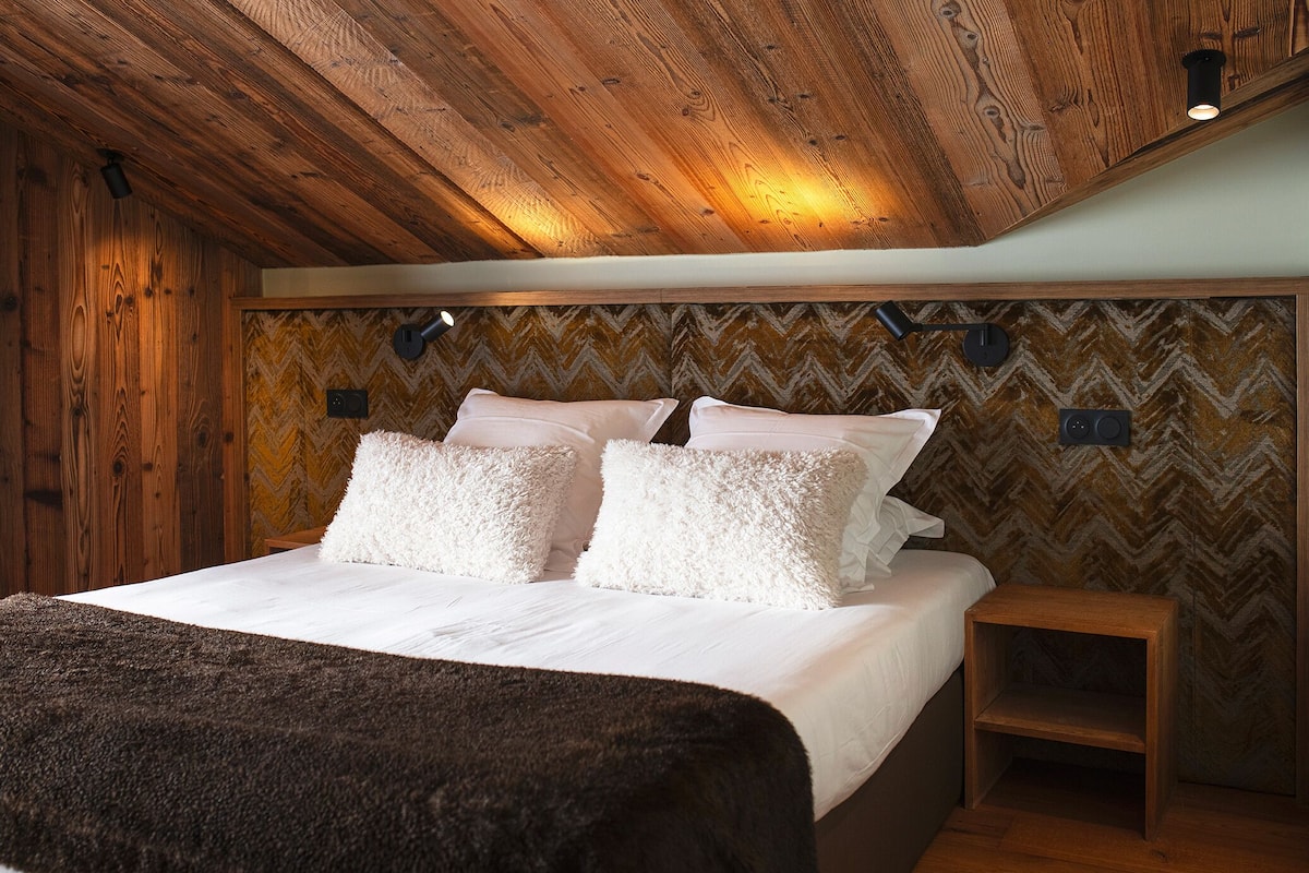 A bedroom with a wooden ceiling, a bed with white bedding, and a herringbone-patterned wall.