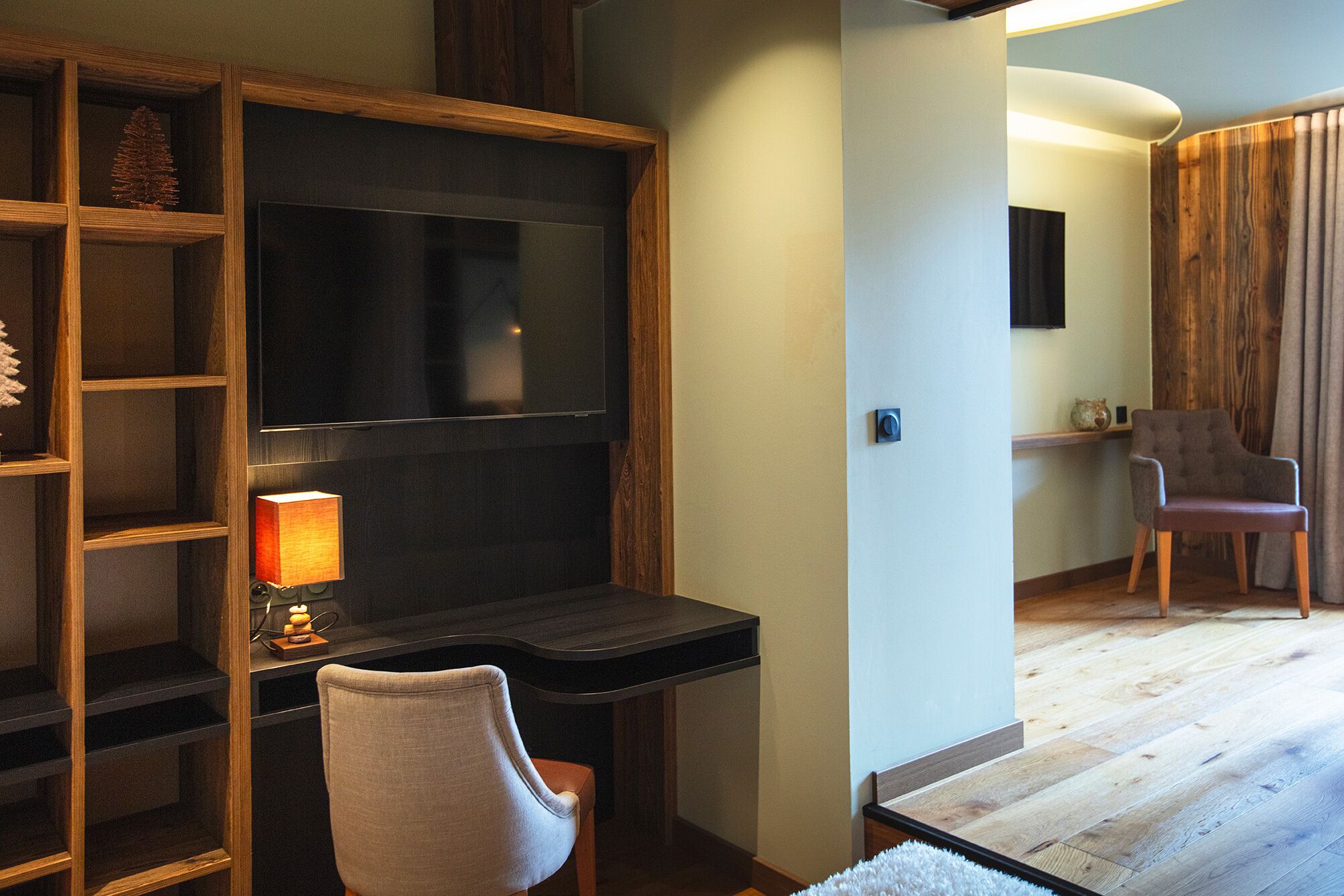 A modern room with a wooden desk, a chair, a TV, and a lamp.