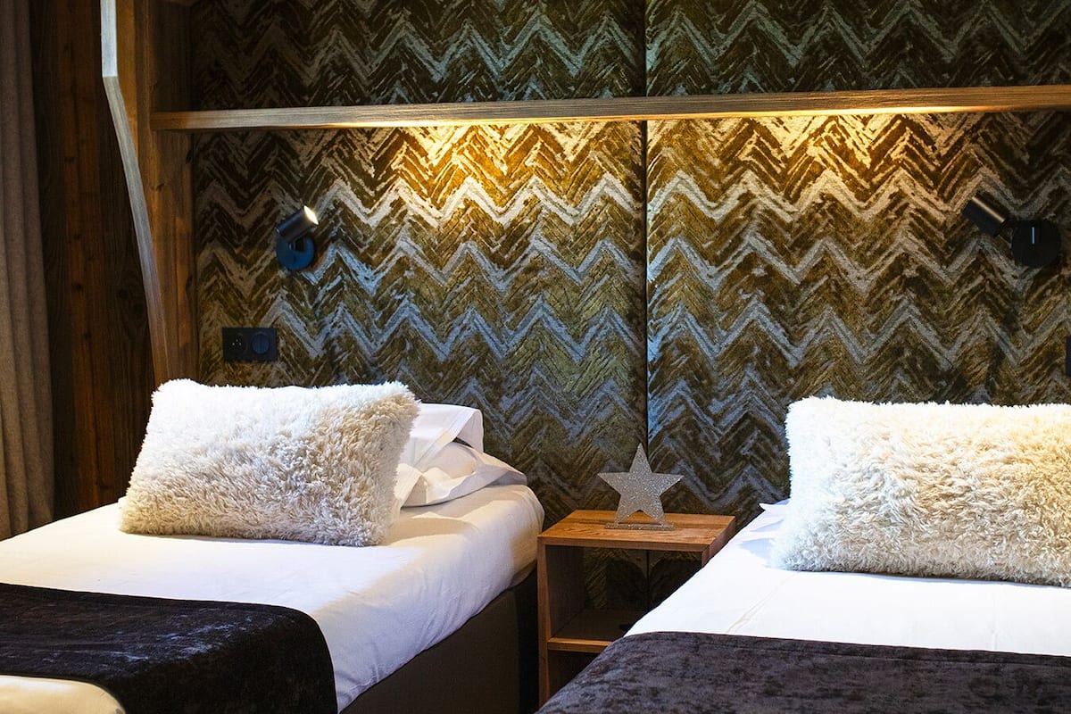 A room with two beds, wooden ceiling, and a chevron-patterned wall.