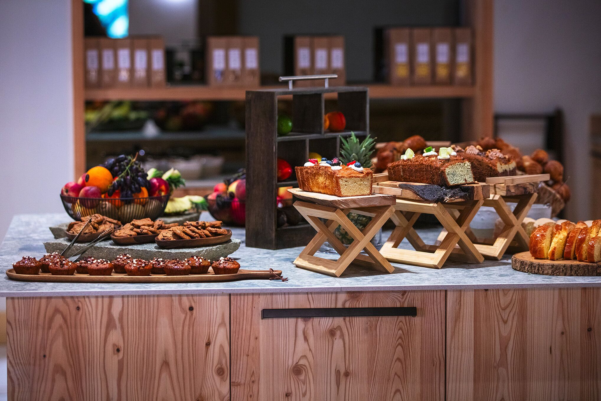 Una barra de madera con diversos productos de panadería y un frutero.