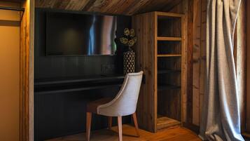 A modern living room with a large flat-screen TV mounted on a dark wall, a wooden chair, and a wooden cabinet with shelves.