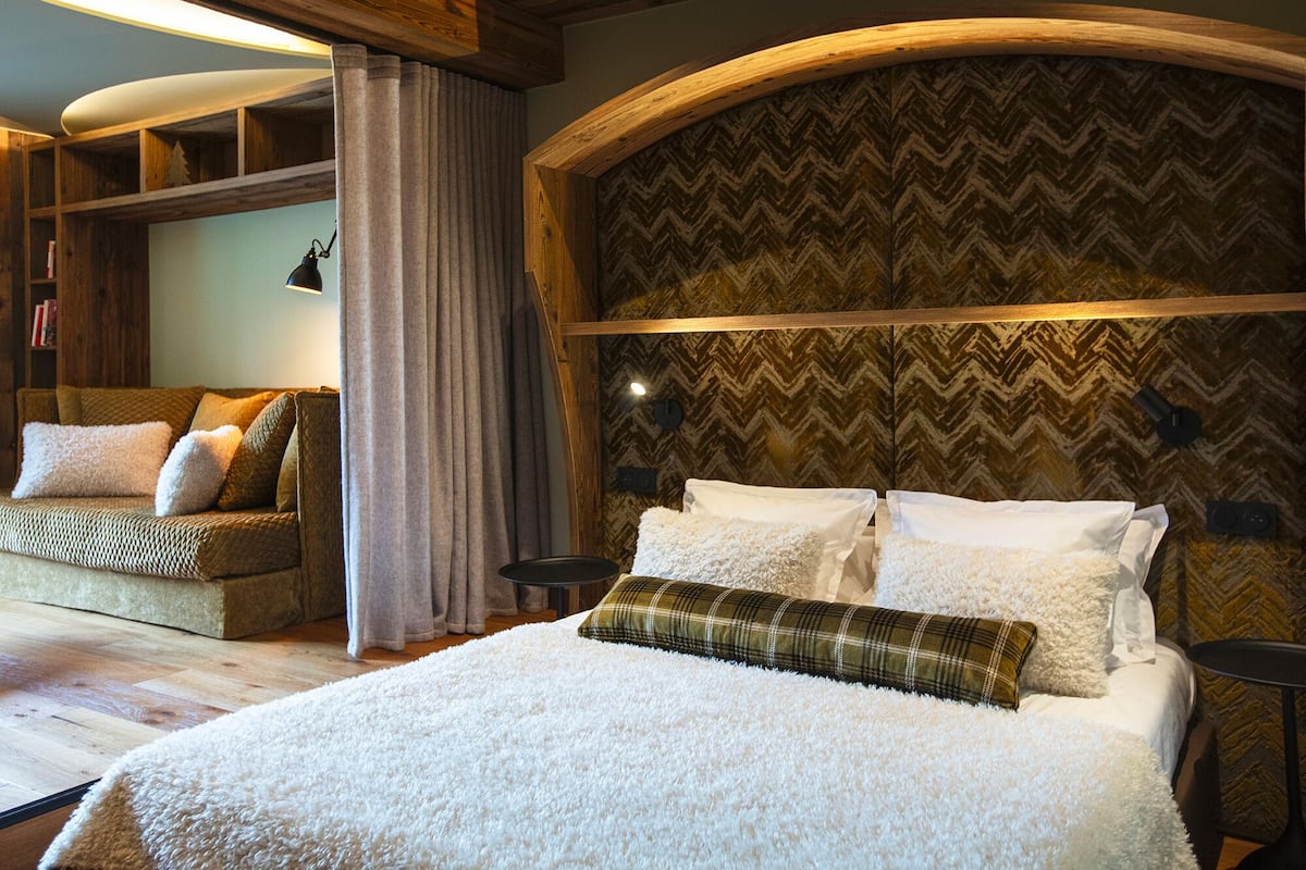 A bedroom with a large bed, a wooden headboard, a built-in shelf, and a cozy seating area with cushions.