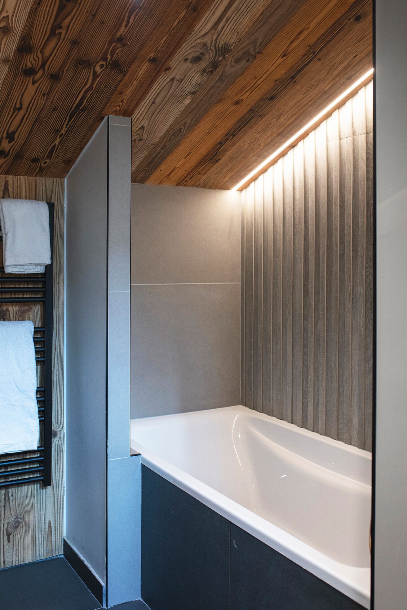 A modern bathroom with a wooden ceiling, a white bathtub, and a towel rack.