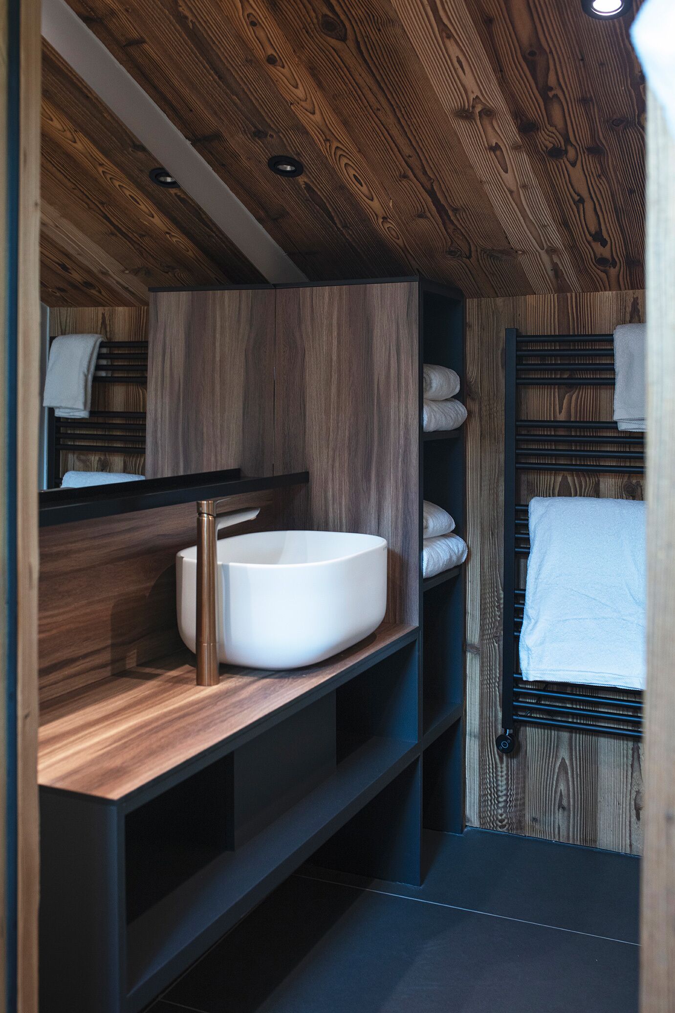 A modern bathroom with a wooden ceiling, a white sink, and built-in shelves.