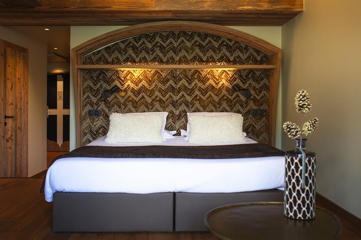 A large bed with a herringbone-patterned headboard, two pillows, and a bedside table with a patterned vase.