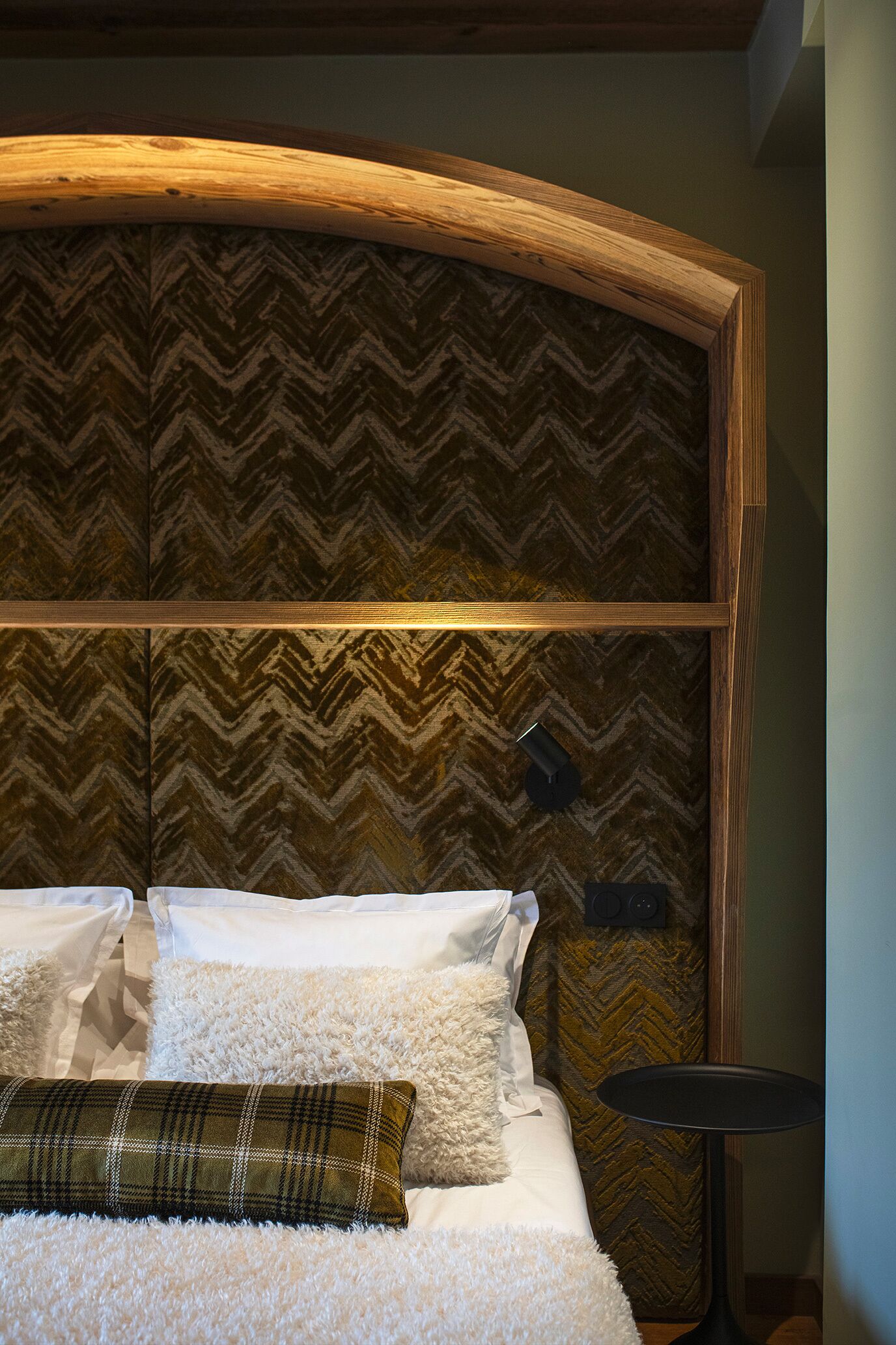 A neatly made bed with white and fluffy bedding, a plaid pillow, and a wooden headboard with a chevron pattern.