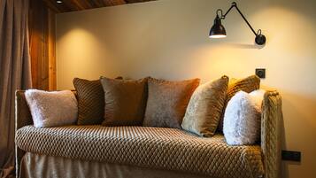 A cozy sofa with a quilted pattern and multiple cushions, a wall-mounted lamp, and wooden ceiling beams.