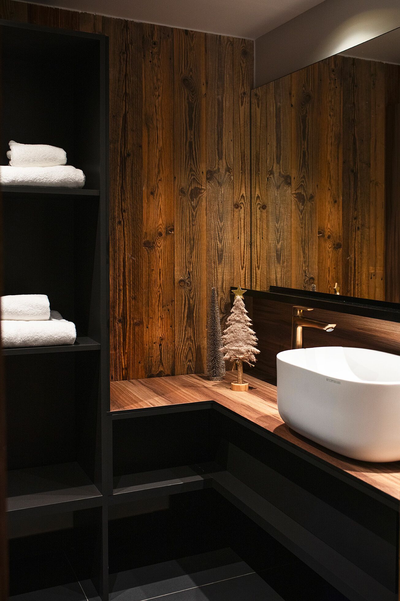 Un baño moderno con paneles de madera, un lavamanos blanco y un pequeño árbol de Navidad.
