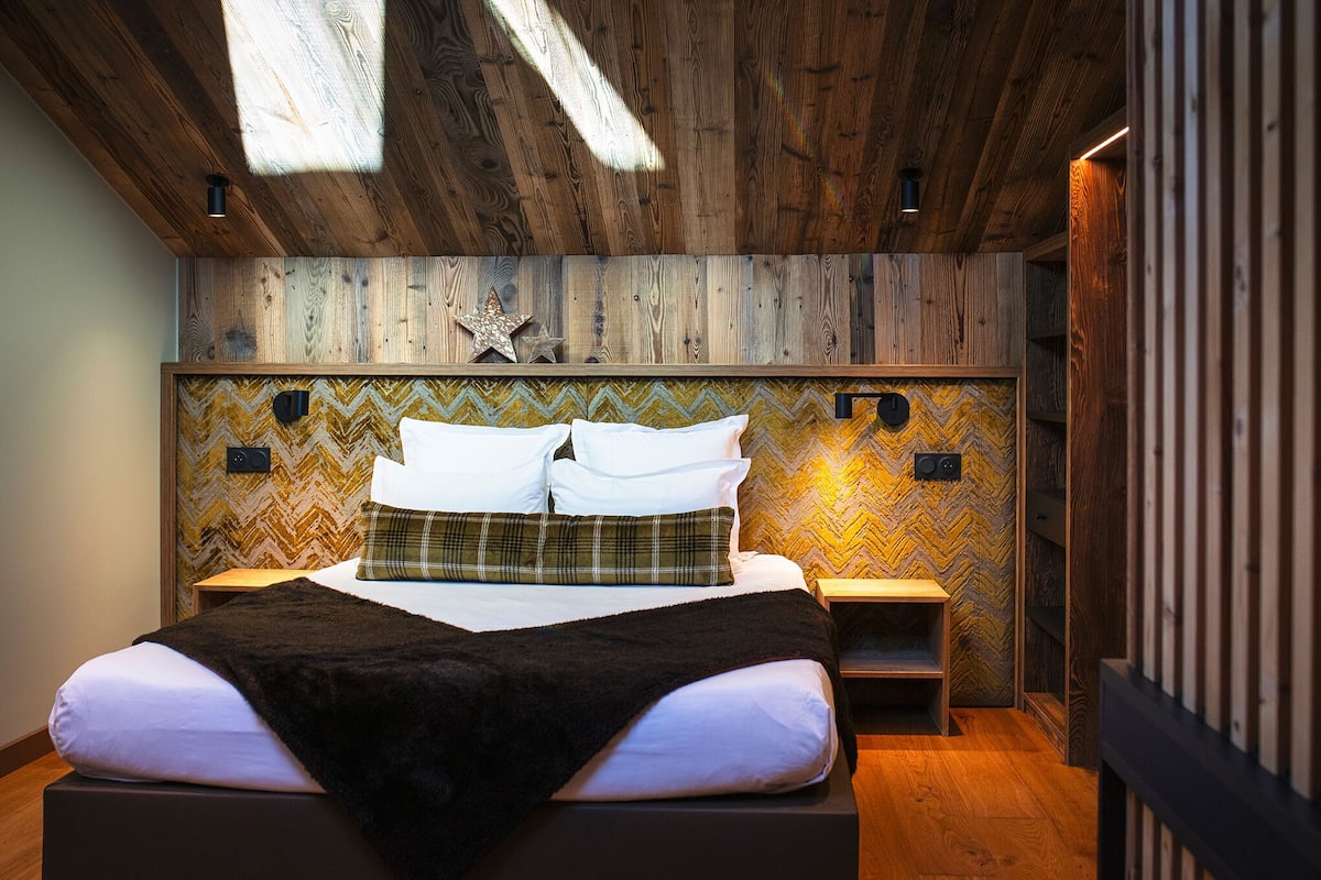 A modern bedroom with a wooden ceiling, a bed with white and plaid bedding, and a chevron-patterned wall.