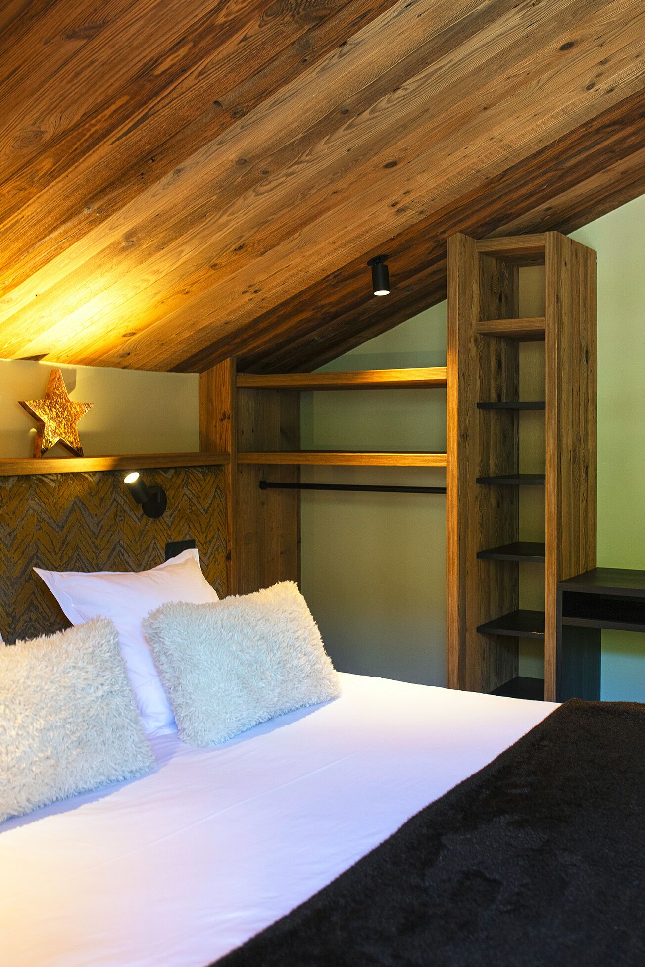 A bedroom with a wooden ceiling, a bed with white and fluffy pillows, a star decoration, and a built-in shelving unit.