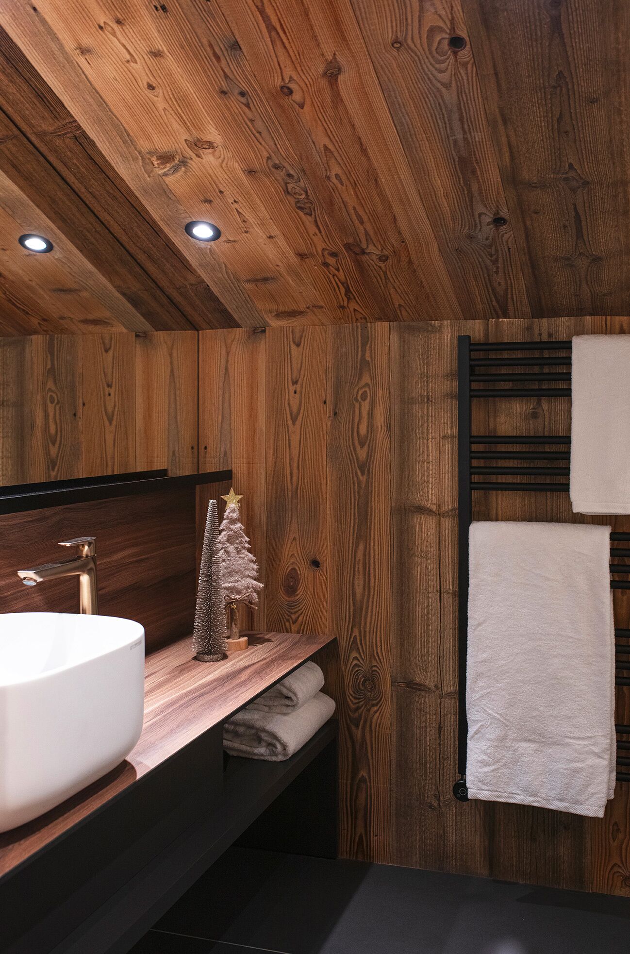 Un baño de madera con un lavamanos grande, un perchero para toallas y un pequeño árbol de Navidad.