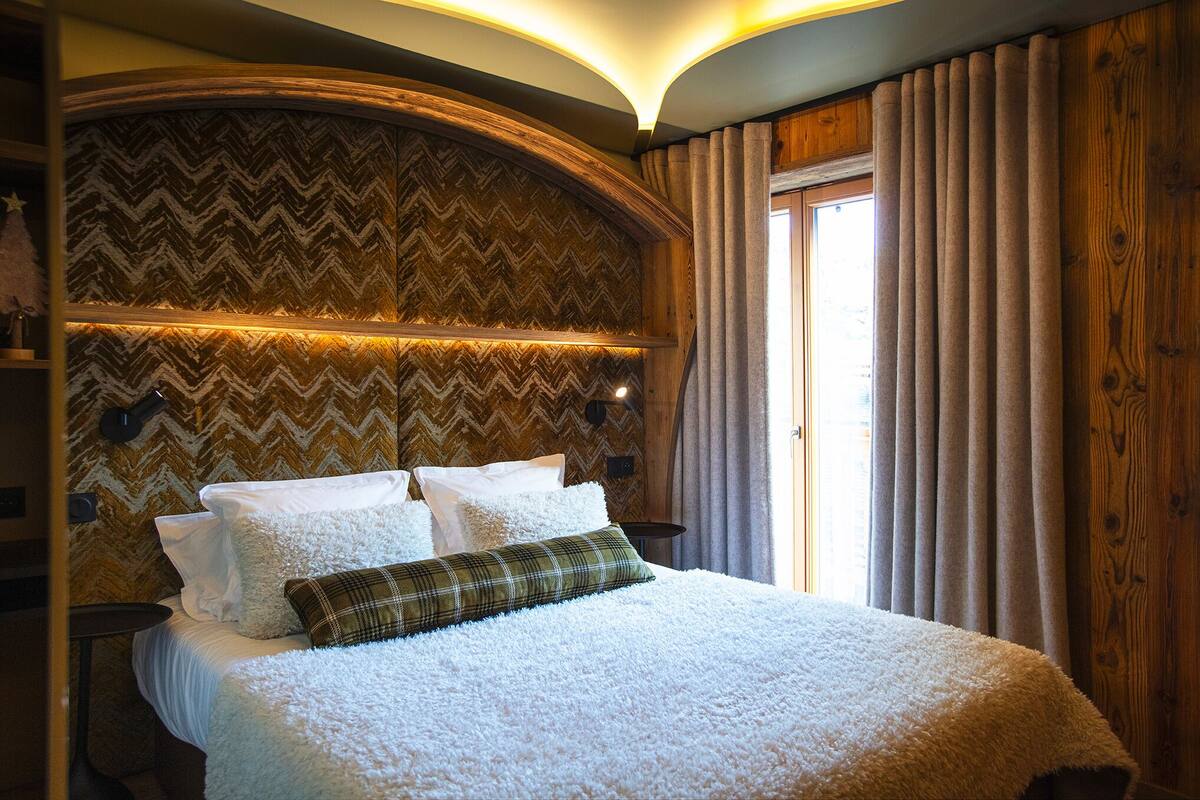 A bedroom with a large bed, wooden headboard, and a window with curtains.
