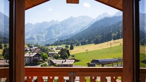 Un balcón de madera con vista a un paisaje montañoso, que incluye casas y un telesilla.