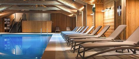 A wooden interior with a swimming pool, sun loungers, and a staircase.