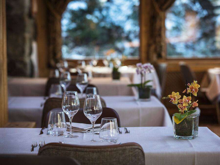 Un restaurante con mesas dispuestas para comer, que incluye cristalería transparente y un pequeño jarrón con flores.