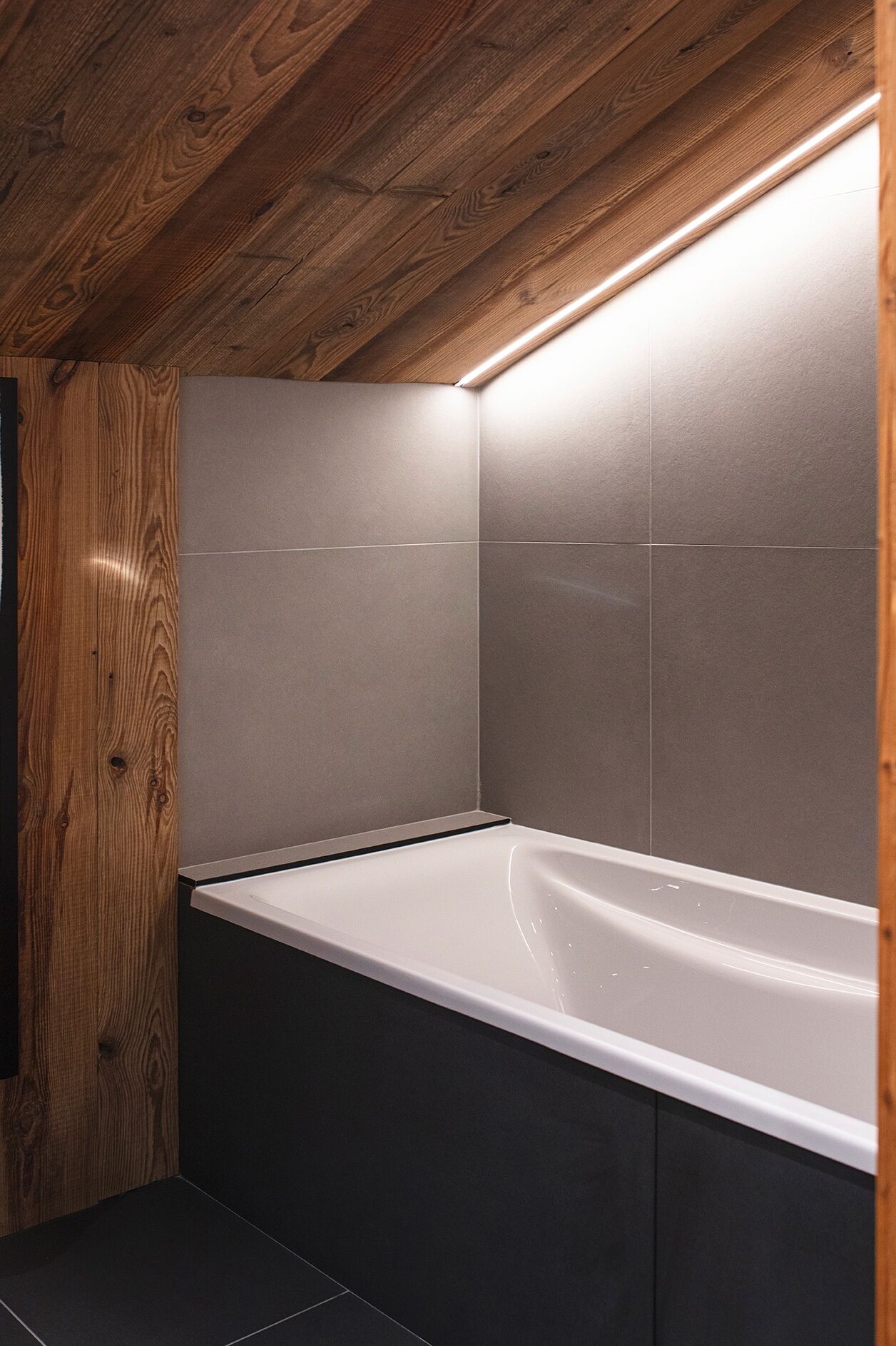 Une salle de bain moderne avec un plafond en bois, une baignoire blanche et des carreaux gris.