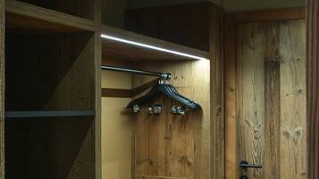 A wooden closet with shelves and a hanging rod, a wooden door, and a small bench.