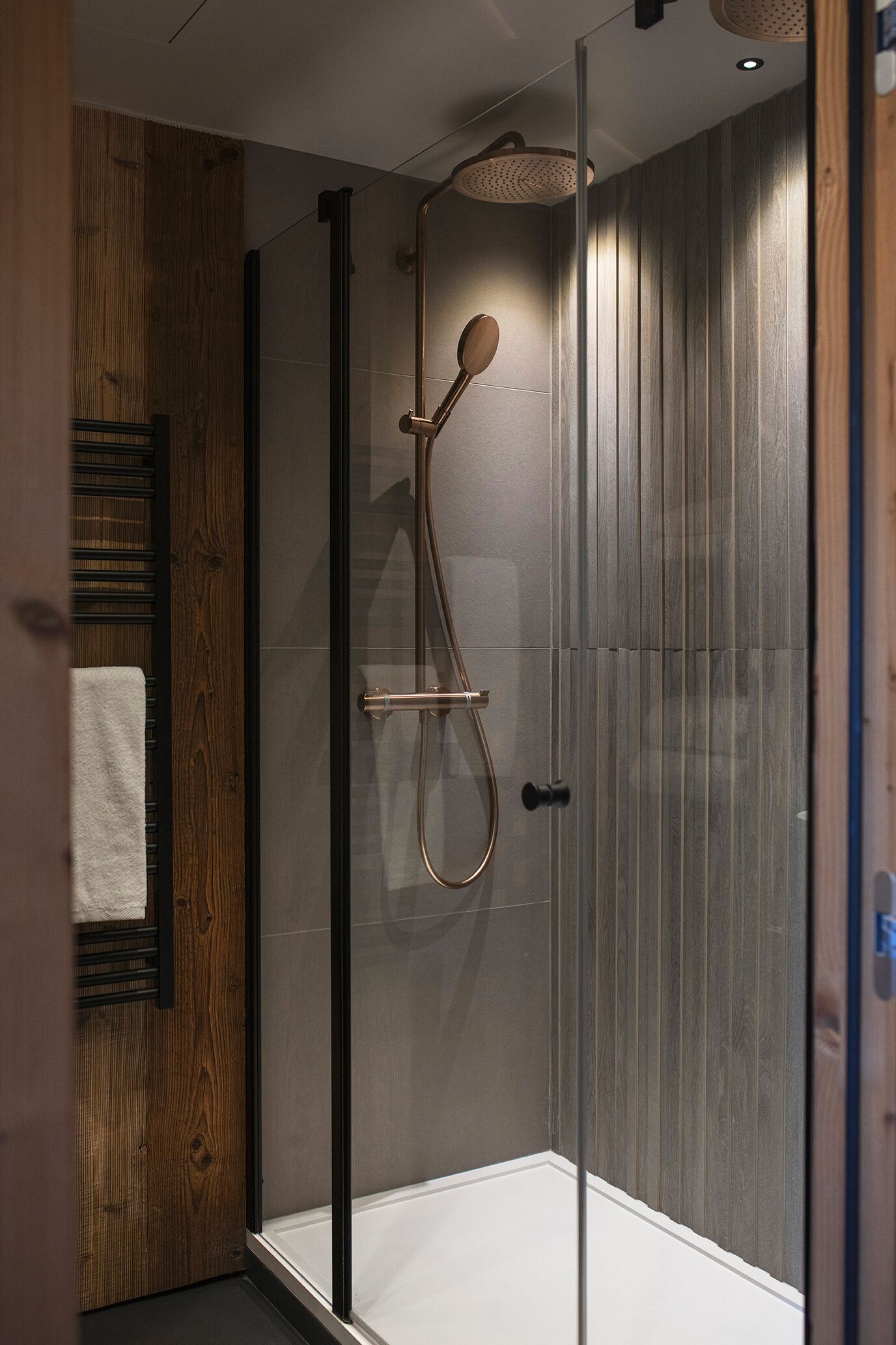 A glass-enclosed shower with a wooden panel wall and a towel rack.
